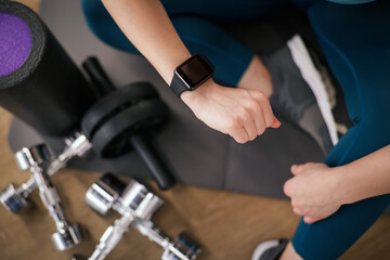 Woman checking fitness tracker during training indoors, top view