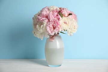 Beautiful peonies in vase on white table near light blue wall