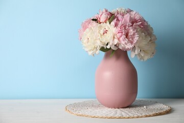 Beautiful peonies in vase on white table near light blue wall. Space for text © New Africa