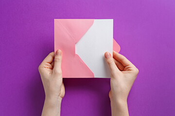 Woman holding envelope with blank invitation card on purple background, top view. Space for design