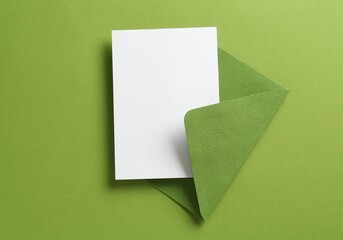 Blank invitation card and envelope on green background, top view. Space for design