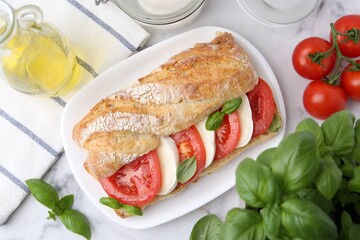 Tasty sandwich with mozzarella cheese, tomatoes and basil on white marble table, flat lay