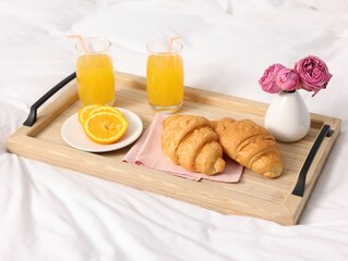 Tray with delicious breakfast and flowers on bed indoors, closeup