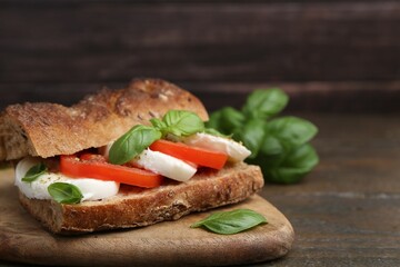 Tasty sandwich with mozzarella cheese, tomatoes and basil on wooden table, closeup. Space for text