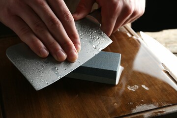 Man sharpening knife with sharpener on wooden table, closeup