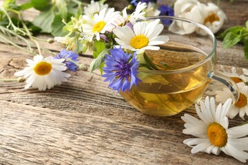 Aromatic herbal tea in glass cup and flowers on wooden table, closeup. Space for text