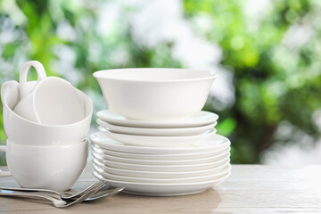 Different clean dishes on wooden table against blurred green background