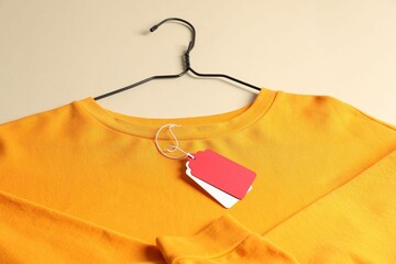 Orange garment with tags on beige background, above view
