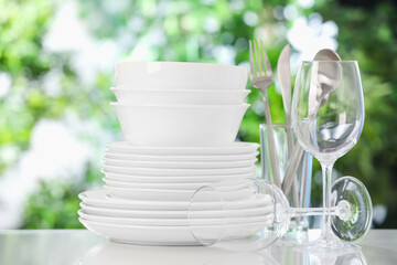 Different clean dishes on white table against blurred green background