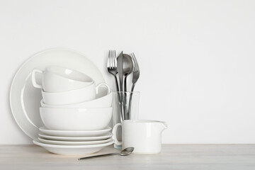 Obraz na płótnie Canvas Different clean dishware on light wooden table near white wall, space for text