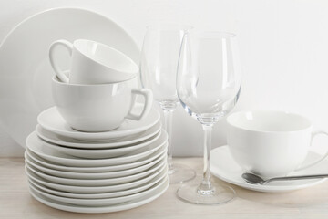 Different clean dishware on light wooden table near white wall