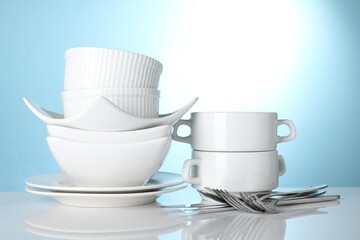 Different clean dishware on white table against light blue background