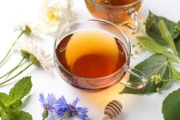 Aromatic herbal tea in glass cups, different flowers and green leaves on white background, closeup