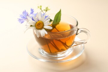Aromatic herbal tea in glass cup and different flowers on beige background, closeup