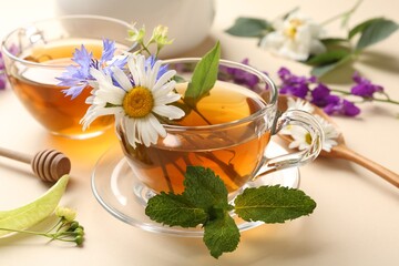 Aromatic herbal tea in glass cups, different flowers and mint on beige background, closeup
