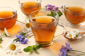 Aromatic herbal tea in glass cups and different flowers on beige background, closeup