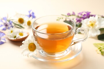 Aromatic herbal tea in glass cup and different flowers on beige background, closeup