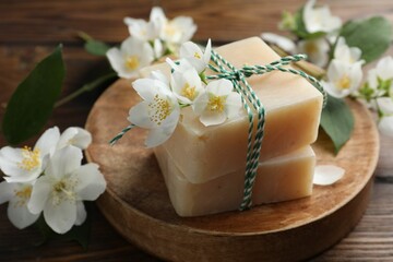 Soap bars and jasmine flowers on wooden table, closeup