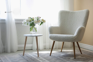 Comfortable armchair and table with vase of flowers near window indoors. Interior design