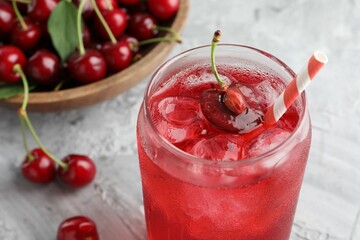 Tasty cherry soda with ice cubes and berries on grey textured table, closeup