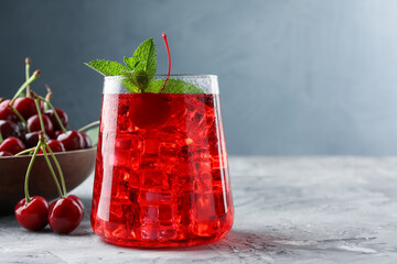 Tasty cherry soda with ice cubes, berries and mint on grey textured table, closeup. Space for text