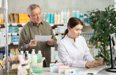 Obraz premium Young woman pharmacist giving prescription pills to elderly man buyer in pharmacy