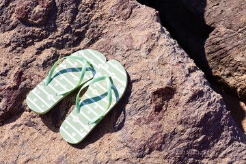 A pair of green flip-flops with white daisy patterns resting on a rough textured rock near the...