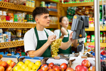 Male shopping assistant weighing grapes in grocery shop