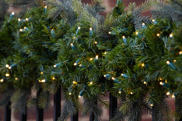 strings of LED christmas lights in pine branches draped around an outdoor railing, decoration for...