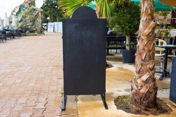 Wooden frame chalkboard stands on summer pavement. The concept shows outdoor signage, seasonal business, and blank advertising opportunity. Copy space.