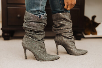 Close-up of sparkly slouchy stiletto boots worn with distressed cuffed denim jeans on a carpeted...
