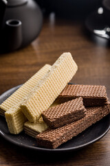 Sweet wafers filled with chocolate and vanilla cream on plate  on wooden table.