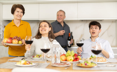 Cheerful young girl sitting at table with husband and senior parents during cozy family celebration...
