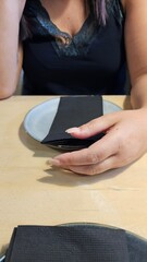 Female hand with manicured nails holding a black napkin over a ceramic plate at a stylish restaurant