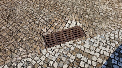 Rusty iron drain grate embedded in traditional calçada portuguesa