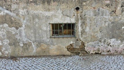 Weathered Old Wall with Small Barred Window and Cracked Plaster