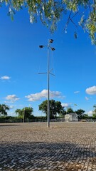 Tall floodlight pole in a large empty cobblestone plaza under clear sky