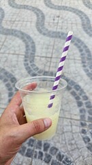 Yellow Slush Drink with Purple and White Straw Held Outdoors