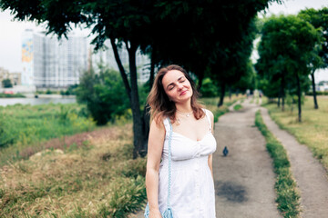 Beautiful girl in a long white dress walking in the park and enjoying summertime.