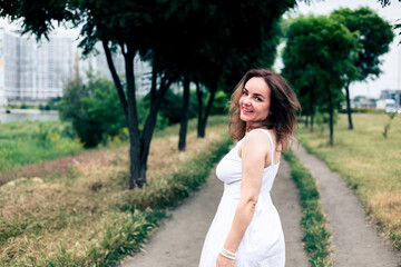 Beautiful girl in a long white dress walking in the park and enjoying summertime.