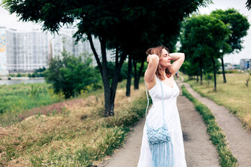 Beautiful girl in a long white dress walking in the park and enjoying summertime.