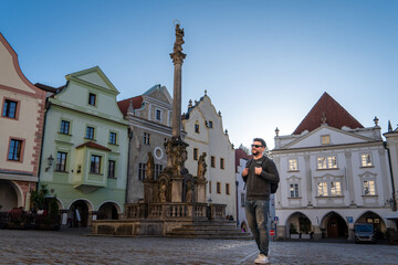Hombre turista paseando por el centro de český krumlov, con la fuente y la columna de la peste de fondo
