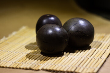 Three Dark Shiny Fruits Resting on Bamboo Mat in Warm Light
