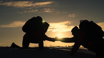 Silhouettes of climbers give each other helping hand, climbing to top of snowy mountain, hill. Traveler climbs snowy peak. Working in team of business people. Team of businessmen is going to win.