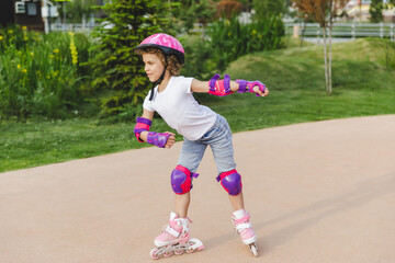 A little curly-haired girl rollerskates within the necessary facilities in the city. In a helmet...