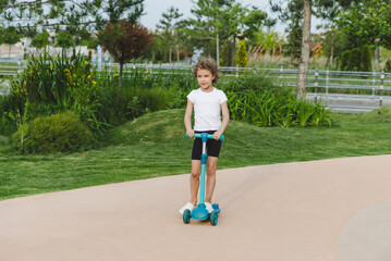 A little curly-haired girl rides a scooter in a city park.