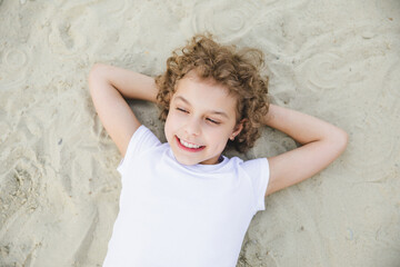little curly blonde girl lies on the sand and smiles.summer portrait