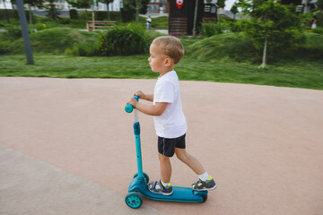A boy of 4-5 years old rides a scooter in a city park.