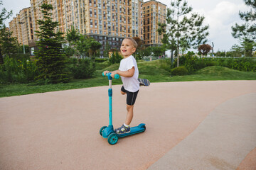 A boy of 4-5 years old rides a scooter in a city park.