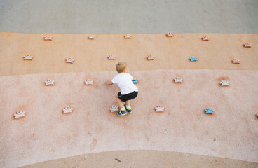 little boy climbing stone wall on playground. sport life concept